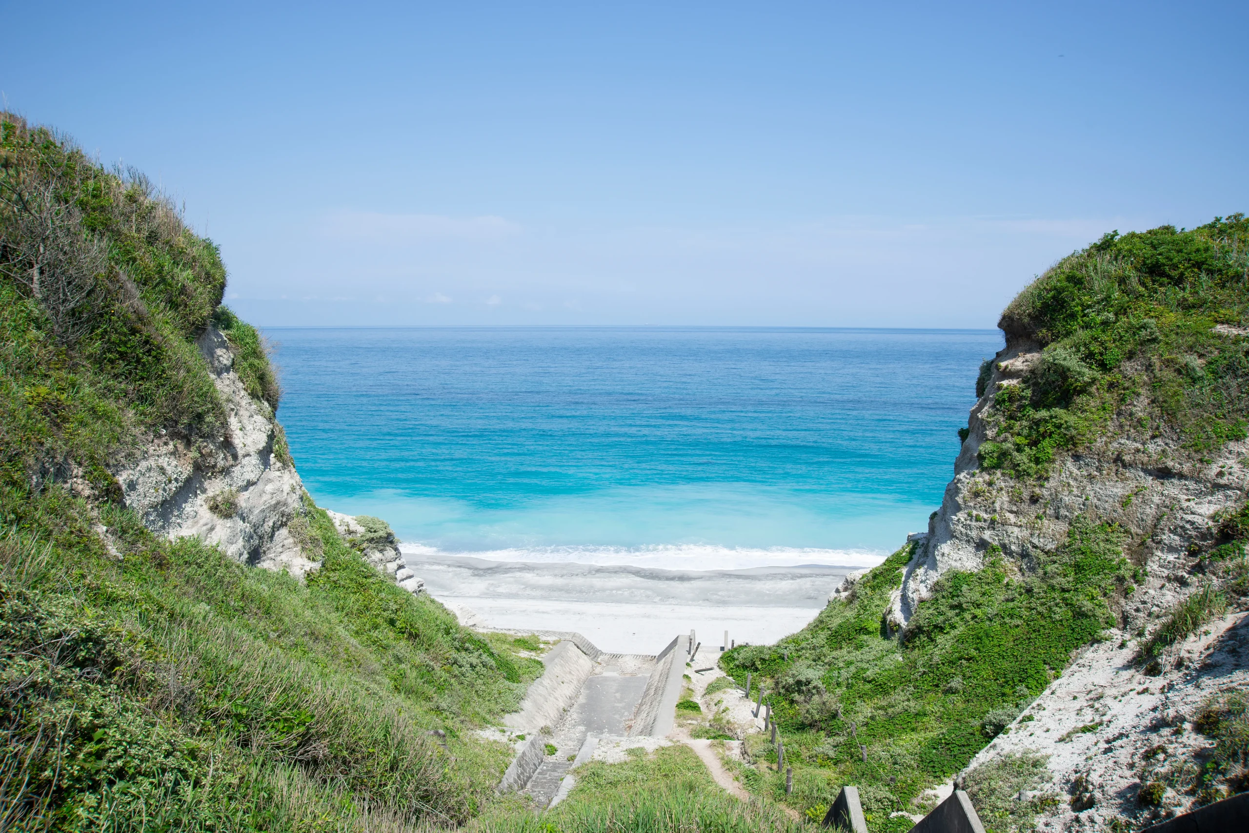 View of the turquoise ocean and white sand beach through cliffs on Niijima Island.