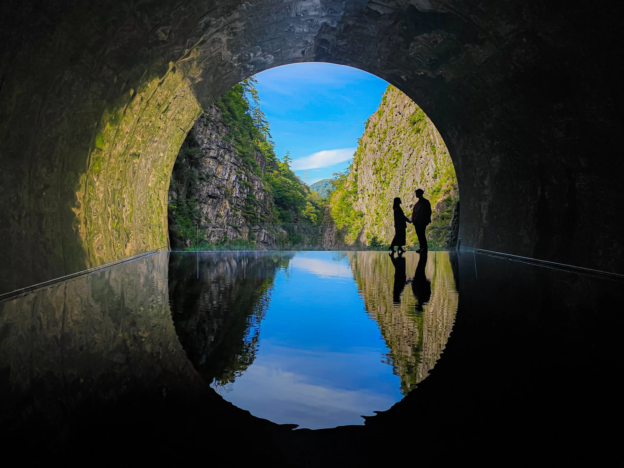 Couple silhouetted at the Tunnel of Light in Kiyotsu Gorge, Niigata, with water reflections.