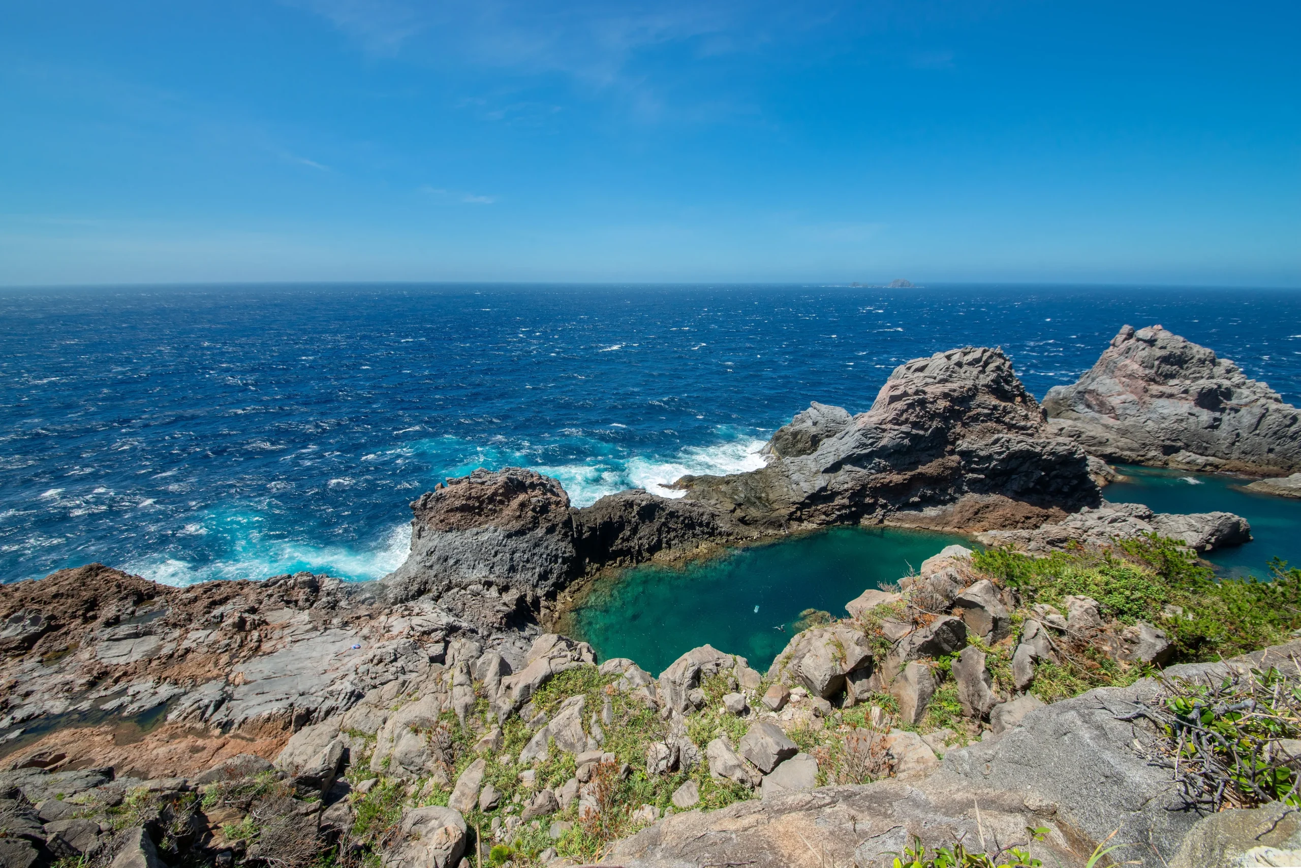 The emerald green Senryoike Pond surrounded by rugged volcanic rocks on Kozushima.