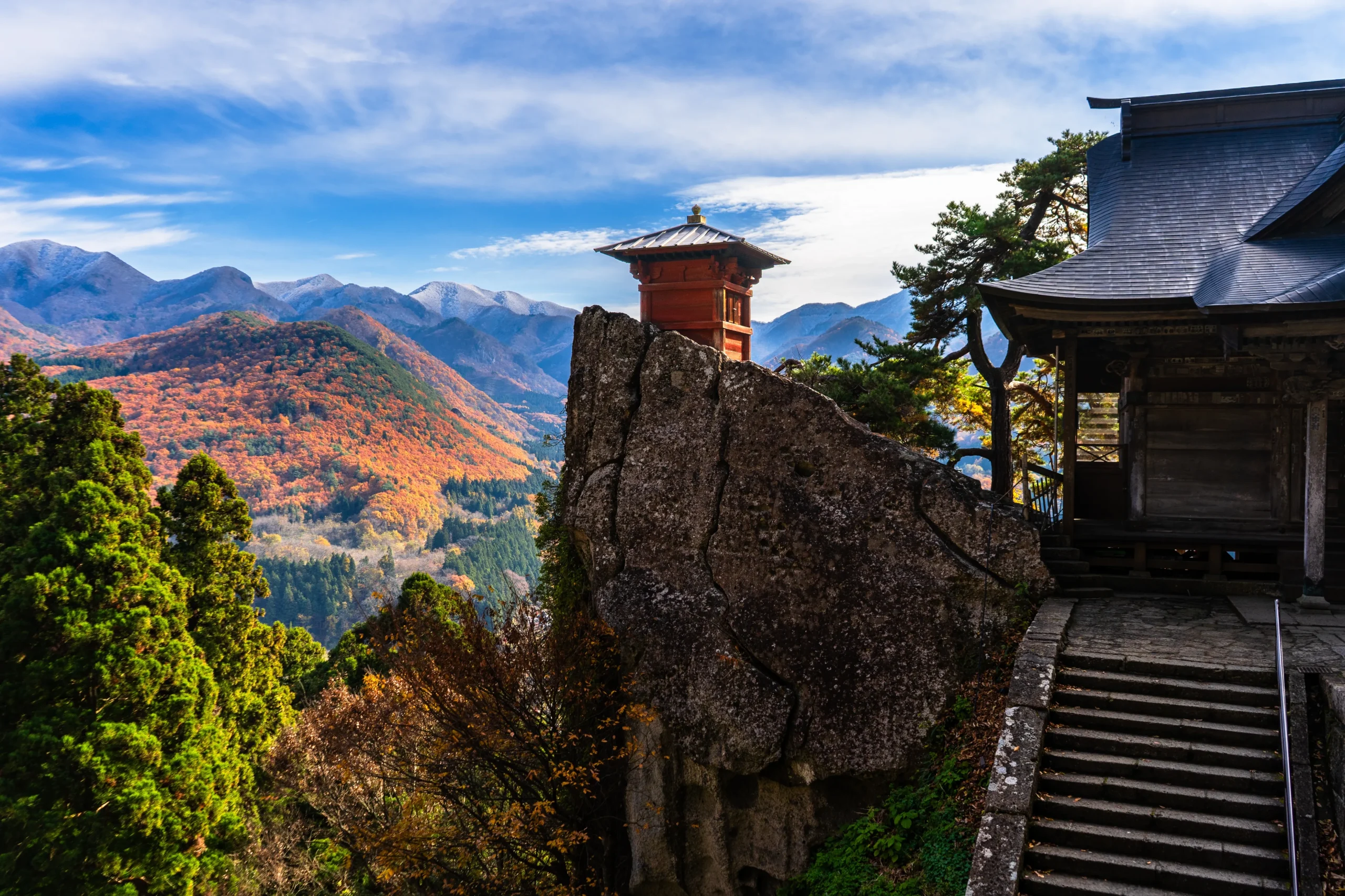 Historic Yamadera Temple buildings perched on a cliffside with autumn mountain views.