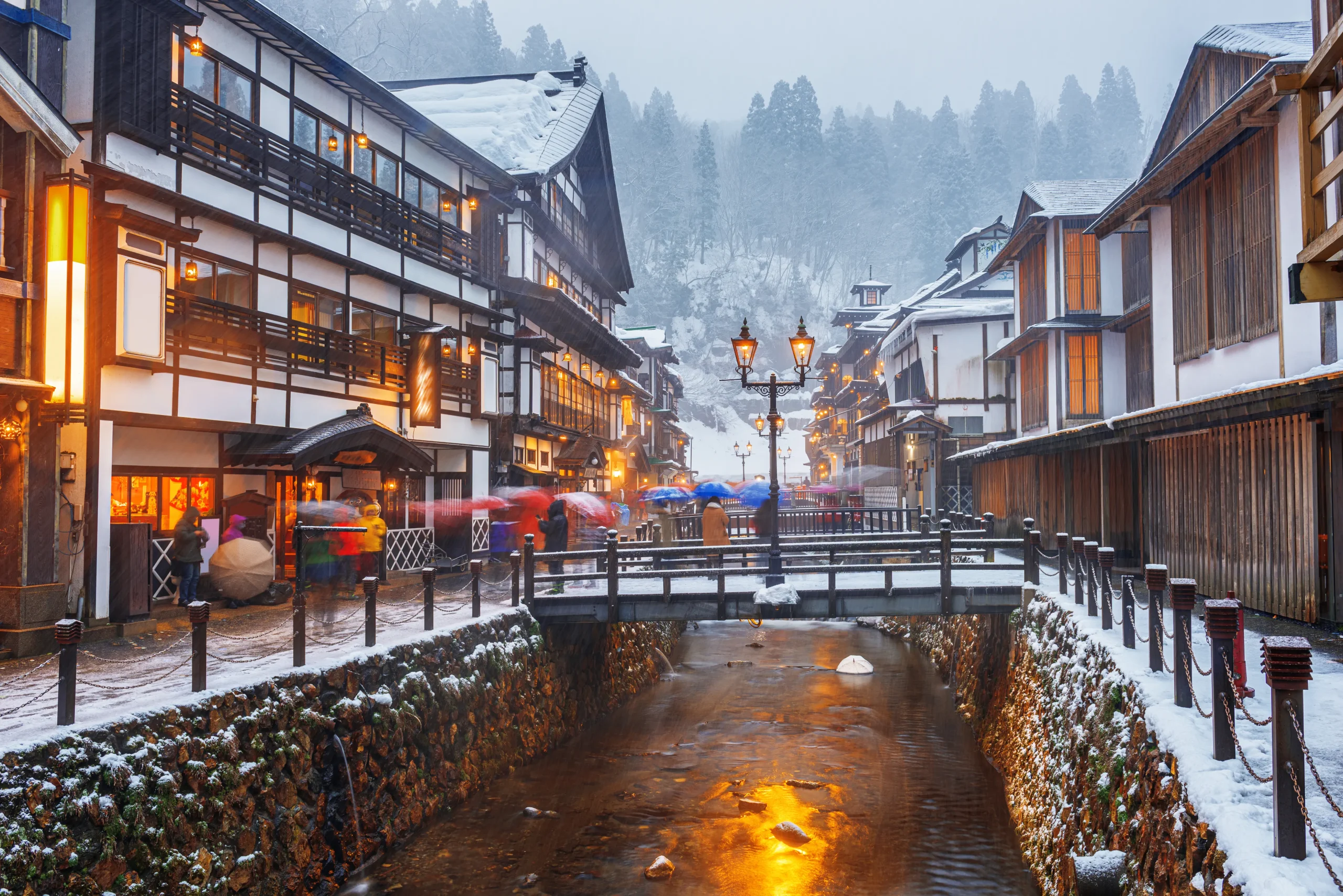 Snowy evening view of traditional ryokan and the river at Ginzan Onsen, Yamagata.