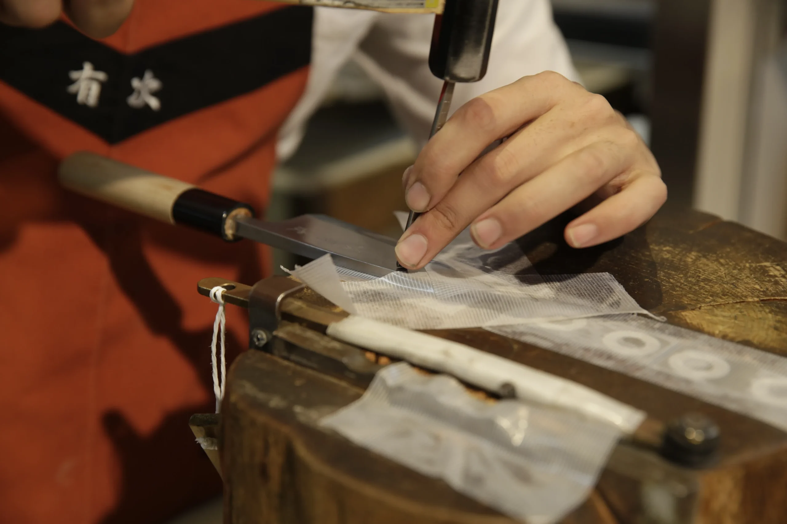 Artisan hand-chiseling a signature on a custom Japanese knife in a traditional workshop.