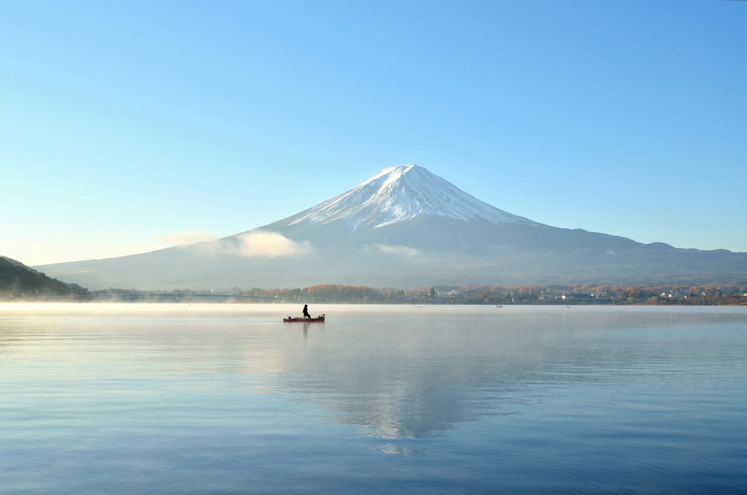 A lone boat on the misty waters of Lake Kawaguchiko with a clear view of Mount Fuji.