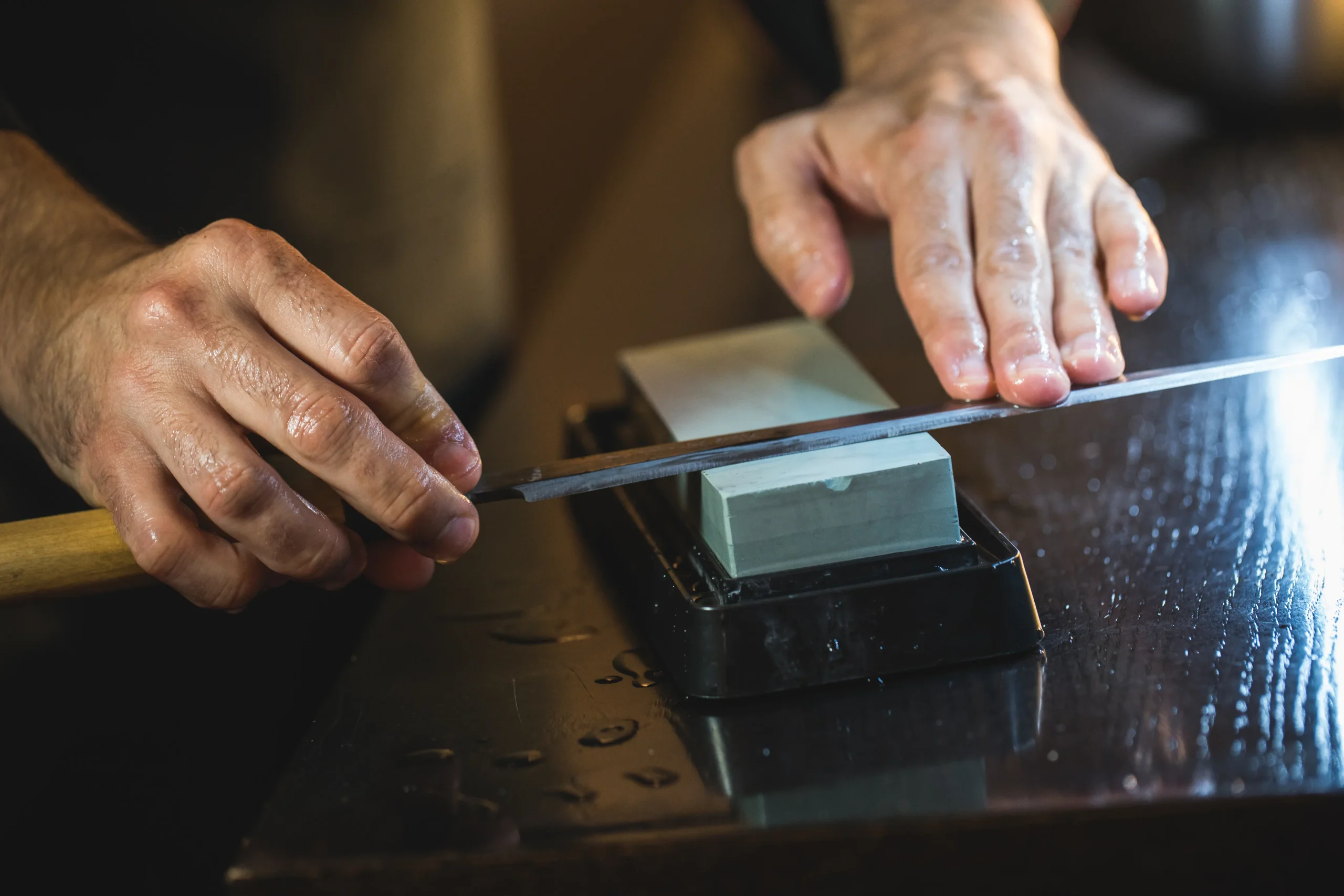 Expert sharpening a high-quality Japanese blade using a traditional whetstone.