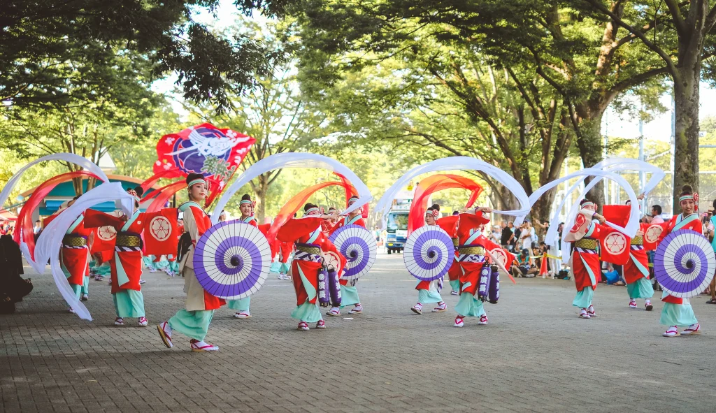 Traditional Yosakoi festival dancers in colorful costumes with umbrellas and banners.