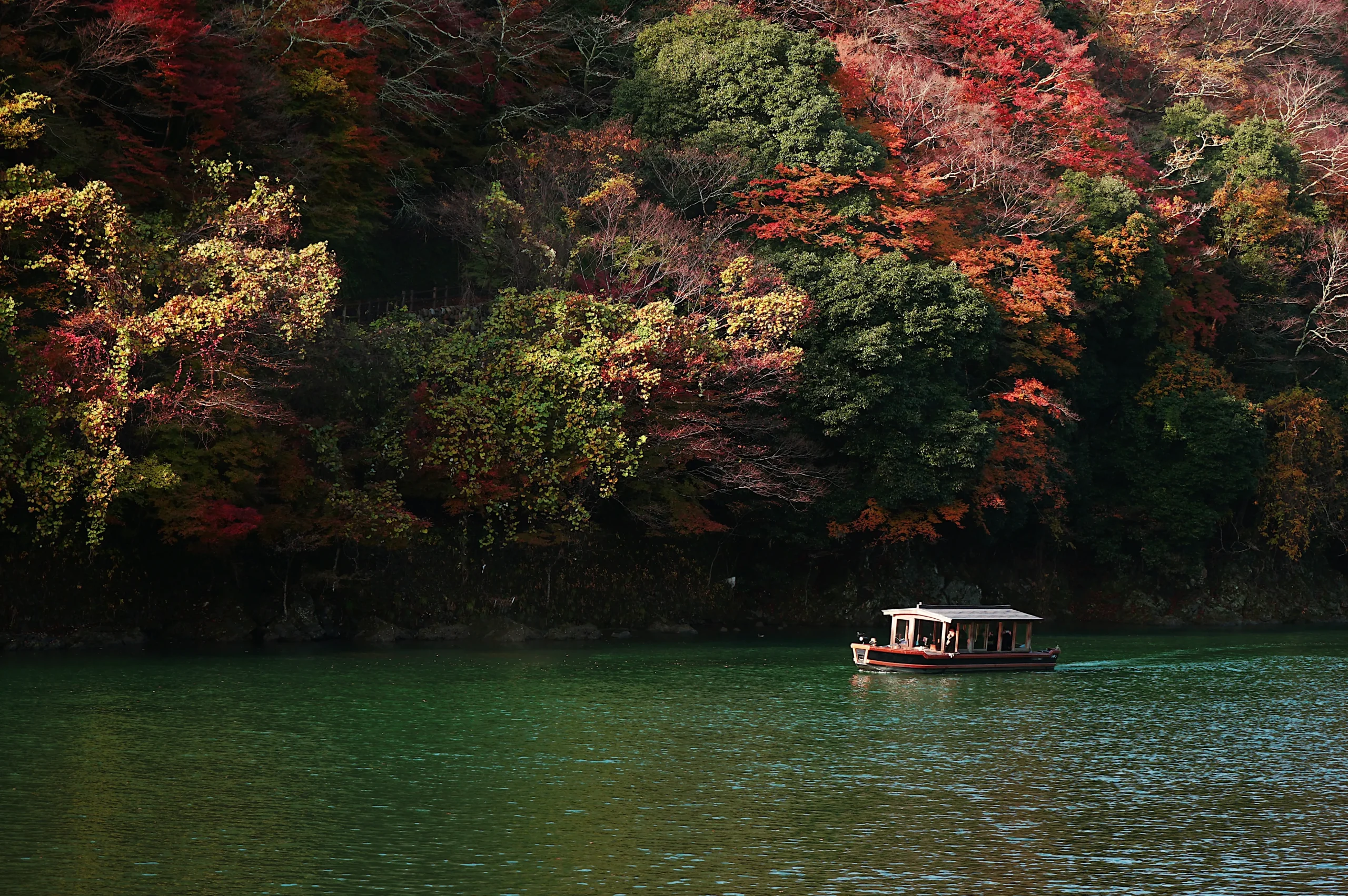 River cruise in Kyoto with boat on calm water surrounded by autumn foliage