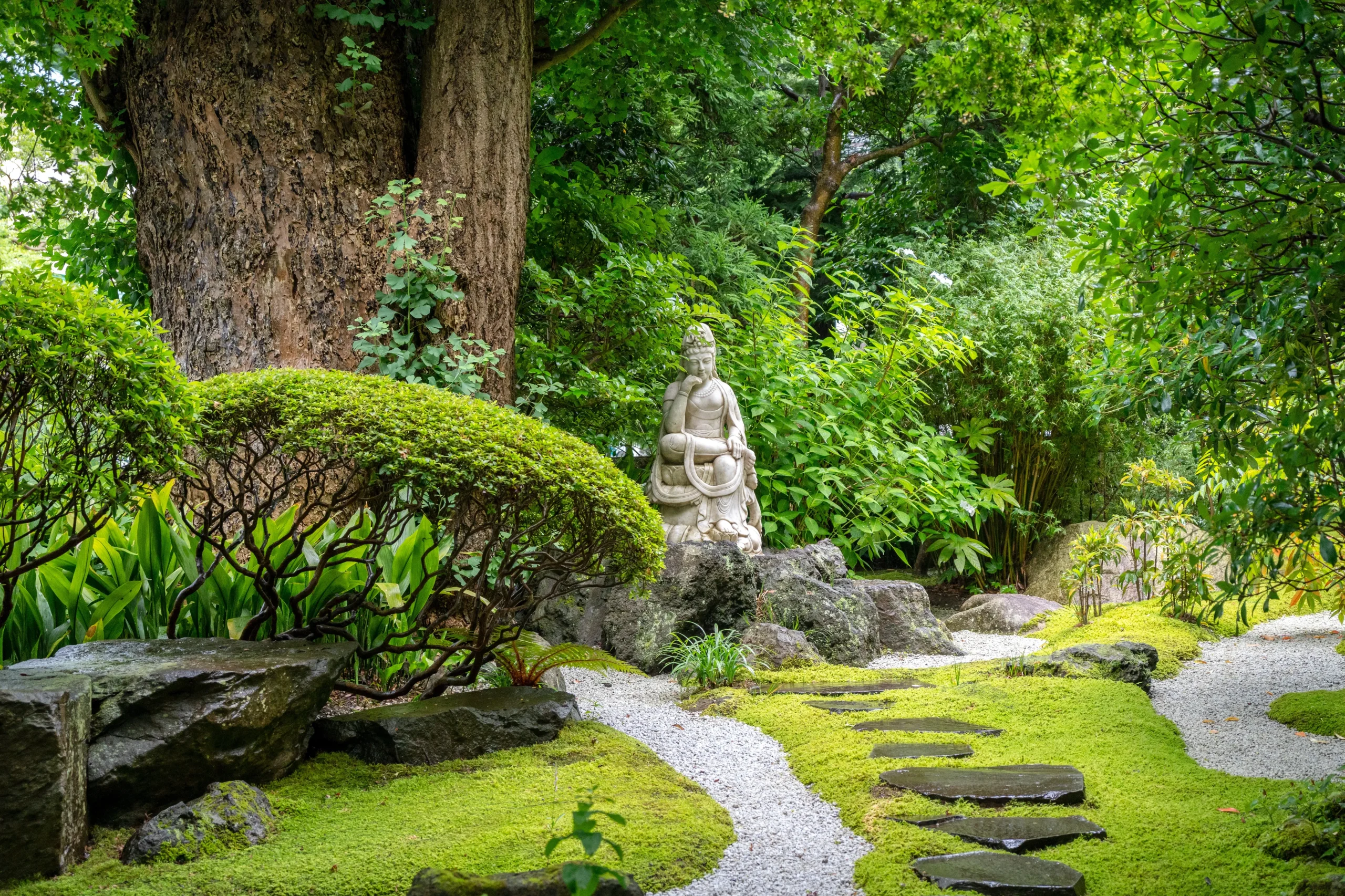 Peaceful Japanese garden at Hokokuji Temple in Kamakura with moss paths, stone steps, and a Buddhist statue surrounded by greenery