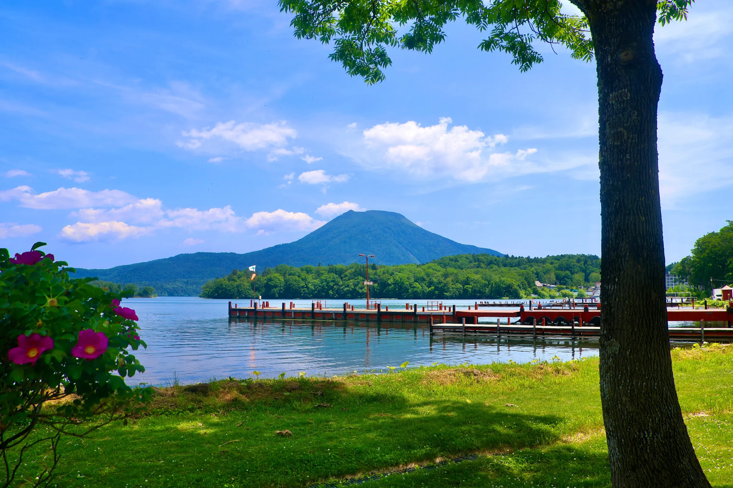 Scenic summer view of Lake Akan in Hokkaido with calm waters, lakeside piers, and Mount Oakan rising in the background