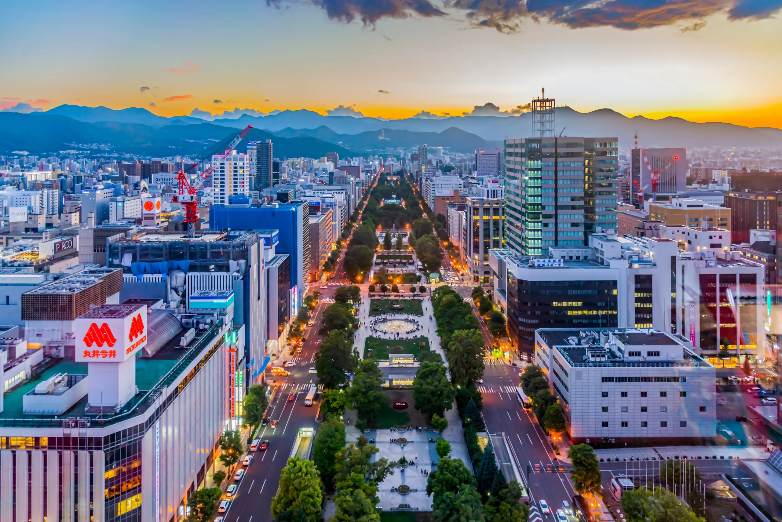 Panoramic sunset view over Odori Park in central Sapporo, surrounded by city buildings and distant mountains