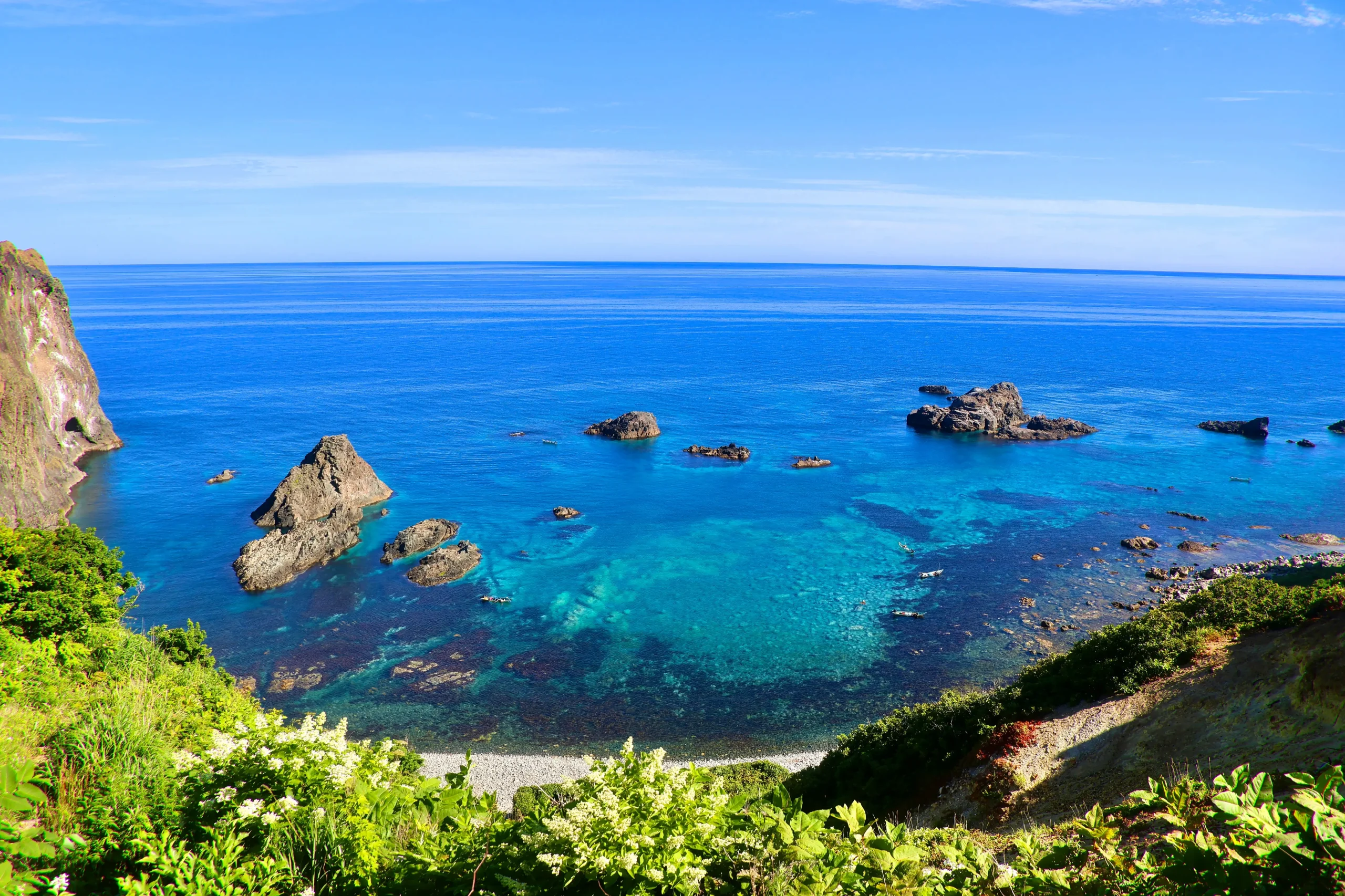 Crystal-clear blue waters and rugged coastline at Shakotan Peninsula in Hokkaido under a bright summer sky