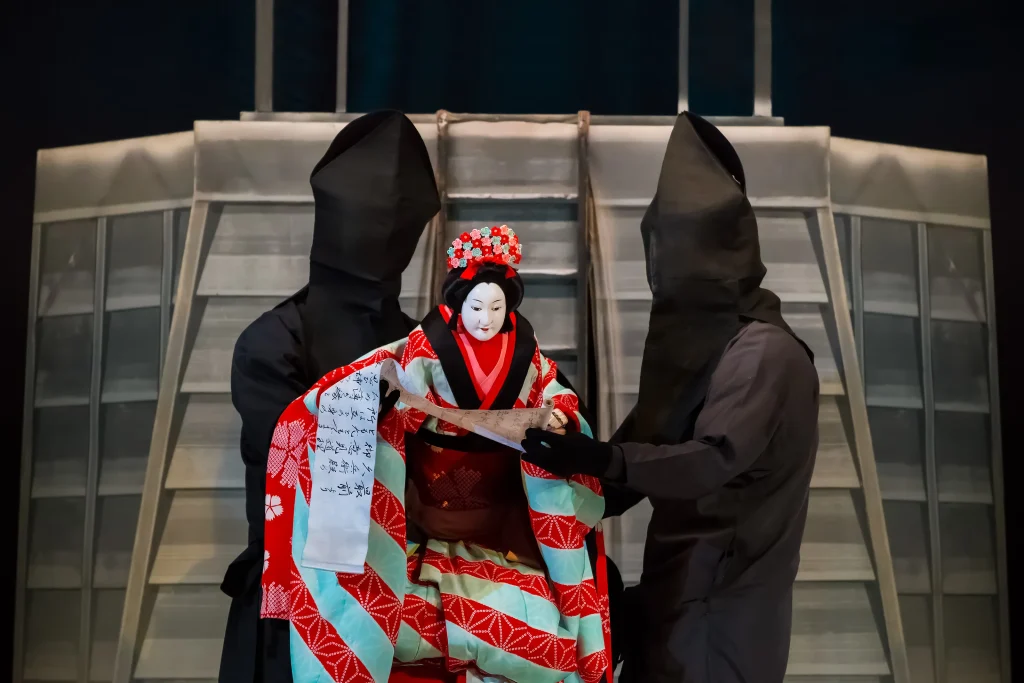 Traditional Japanese Bunraku puppet dressed in an elaborate kimono, operated by masked puppeteers during a classical theater performance