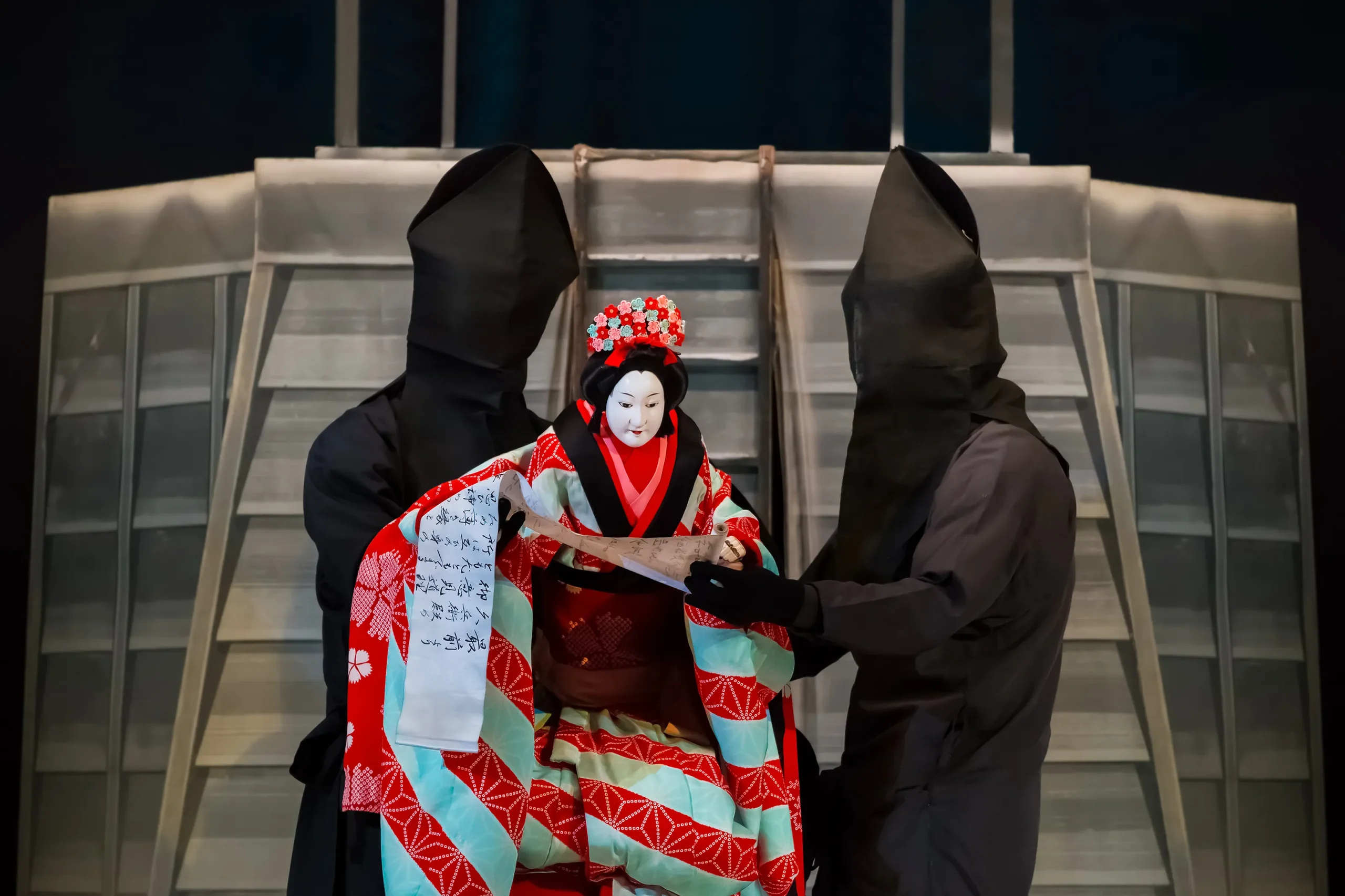 Traditional Japanese Bunraku puppet dressed in an elaborate kimono, operated by masked puppeteers during a classical theater performance