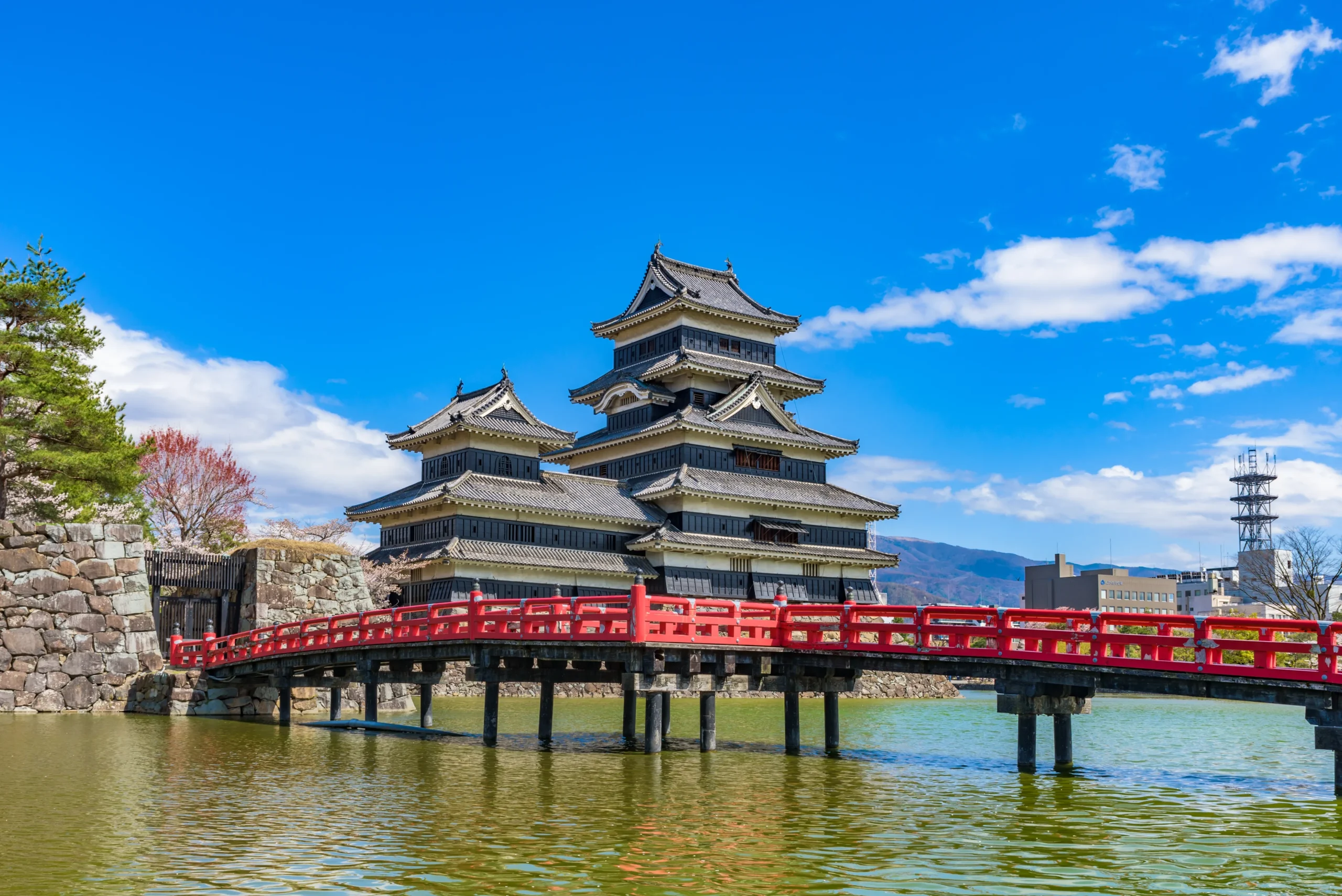 Historic Matsumoto Castle in Nagano reflected across the moat, with its iconic black keep and bright red bridge under a clear blue sky