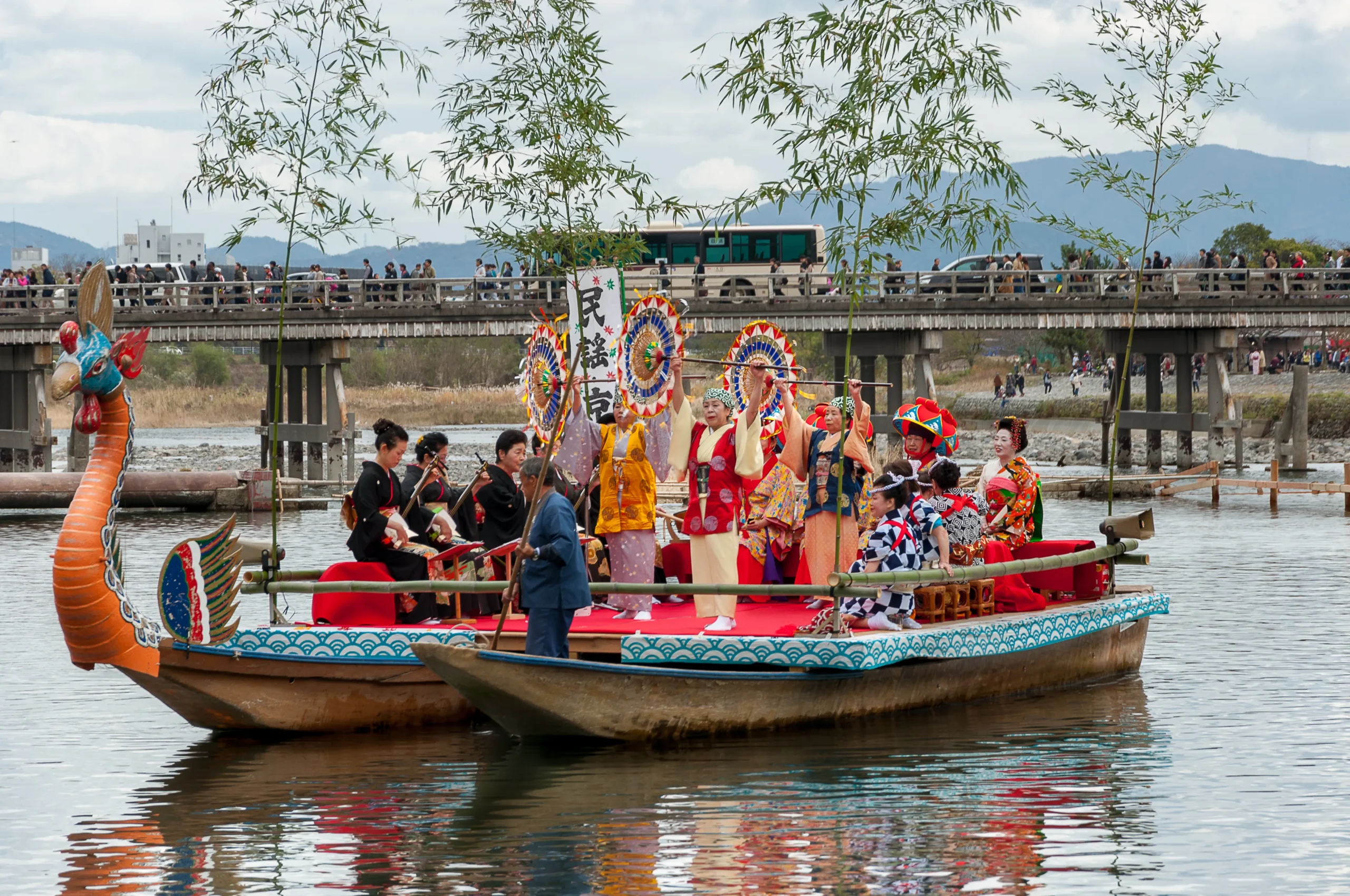 Costumed performers with parasols on a dragon-prow boat during the Arashiyama Momiji Festival in Kyoto.