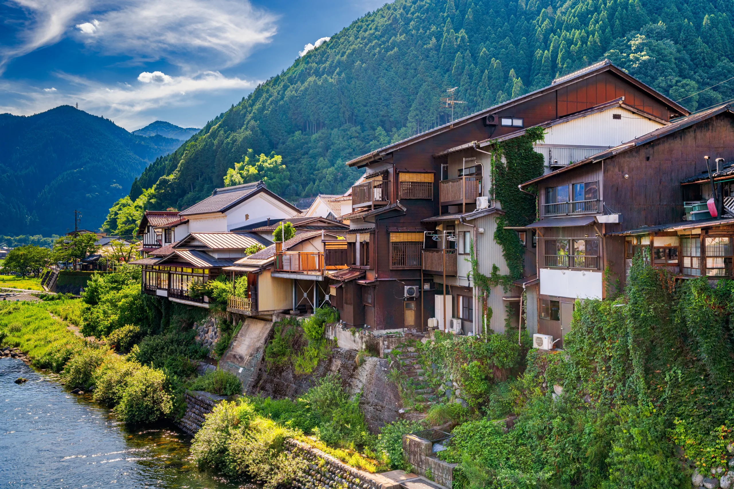 Wooden houses along the riverside below green mountains in Gujo Hachiman, Gifu