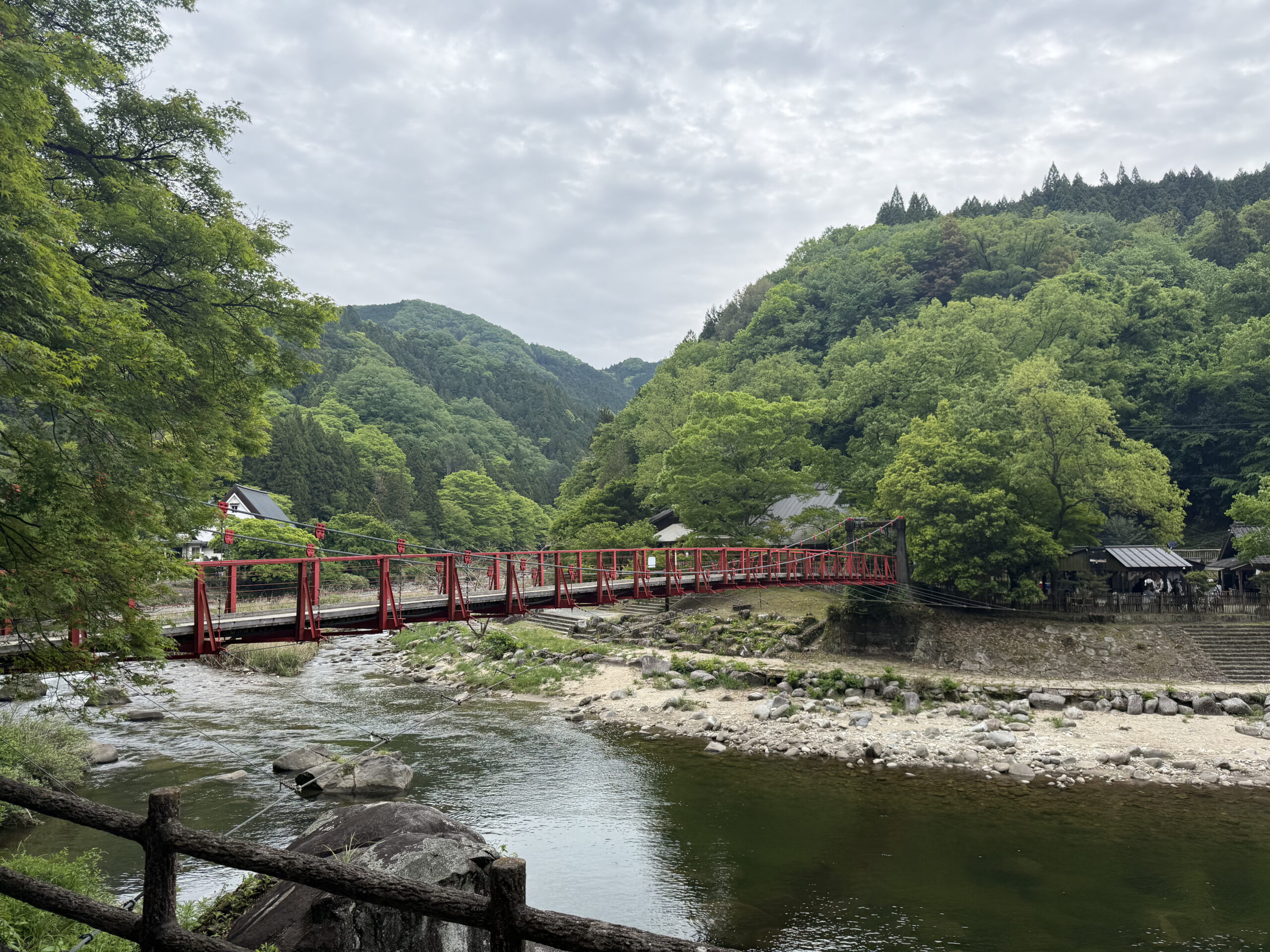 Red suspension bridge over a river surrounded by lush green mountains at Korankei, Aichi
