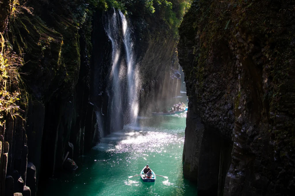 Rowboats on emerald water beneath Manai Falls in Takachiho Gorge, Miyazaki, Japan, framed by basalt cliffs.