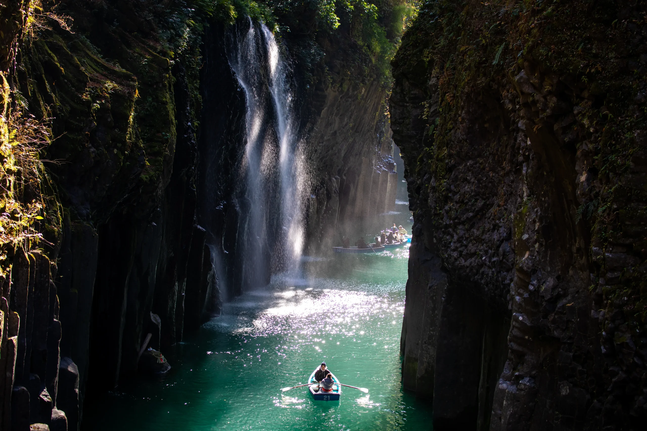 Rowboats on emerald water beneath Manai Falls in Takachiho Gorge, Miyazaki, Japan, framed by basalt cliffs.