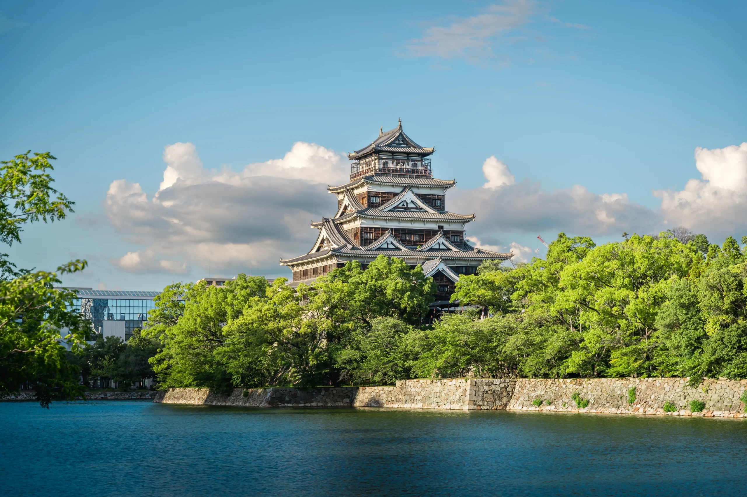 Hiroshima Castle keep rising above green trees and the moat under a blue sky