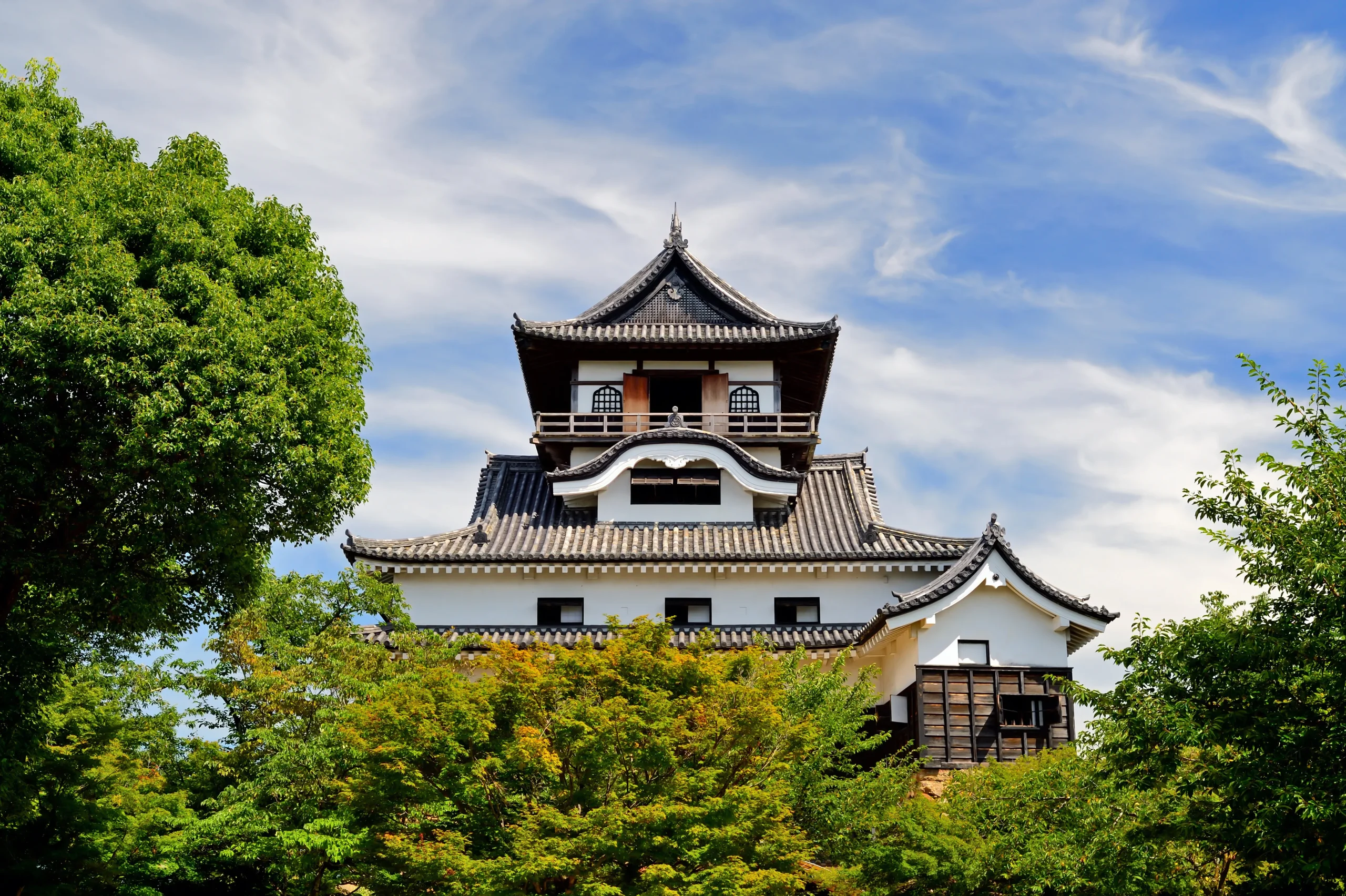 Inuyama Castle keep on a hill surrounded by trees under a blue sky