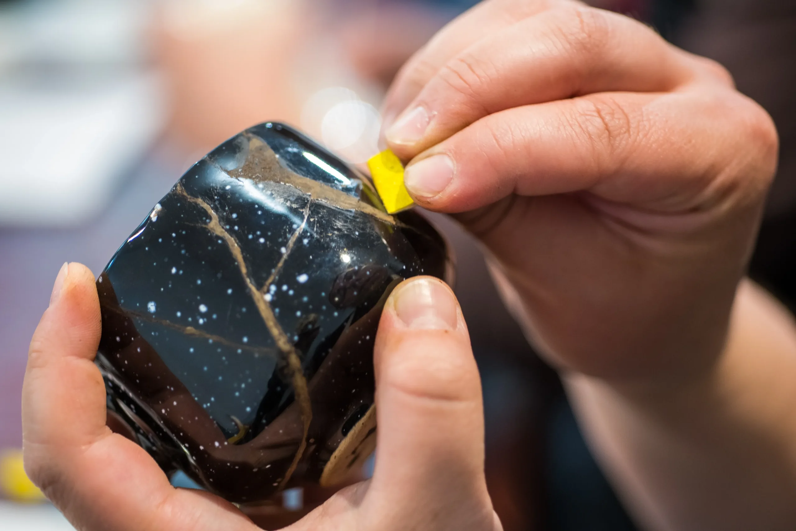 Hands repairing a cracked bowl with gold using the Japanese kintsugi technique