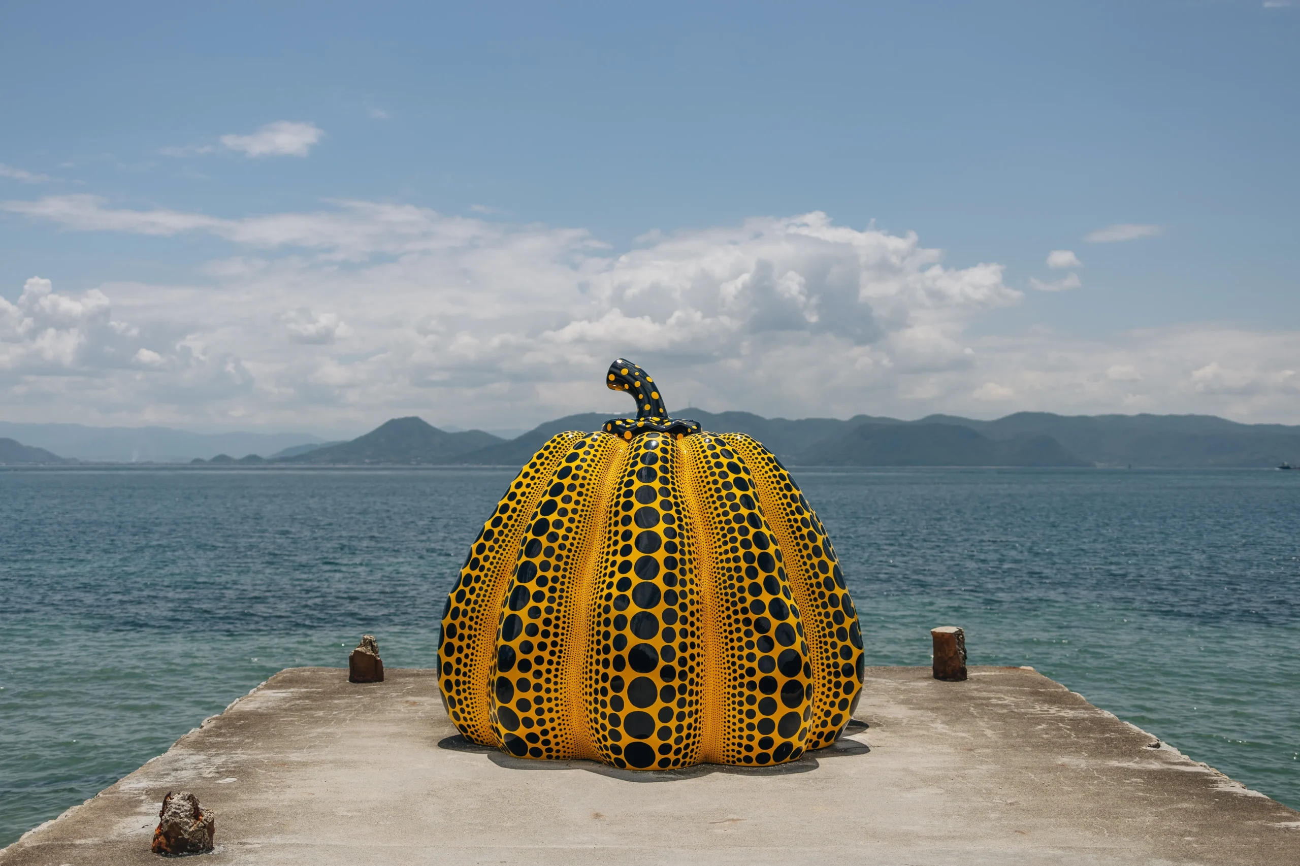 Yellow polka-dot pumpkin sculpture on a pier overlooking the sea on Naoshima