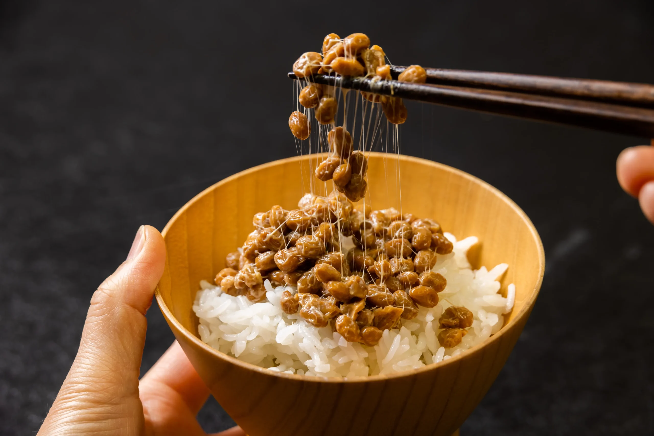 Sticky natto fermented soybeans lifted with chopsticks over steamed rice