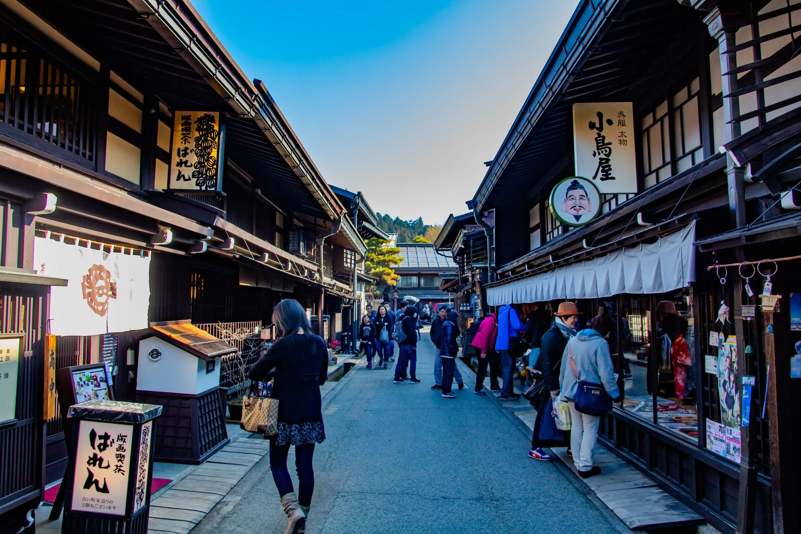 Tourists walking past dark wooden merchant houses in Takayama old town, Gifu