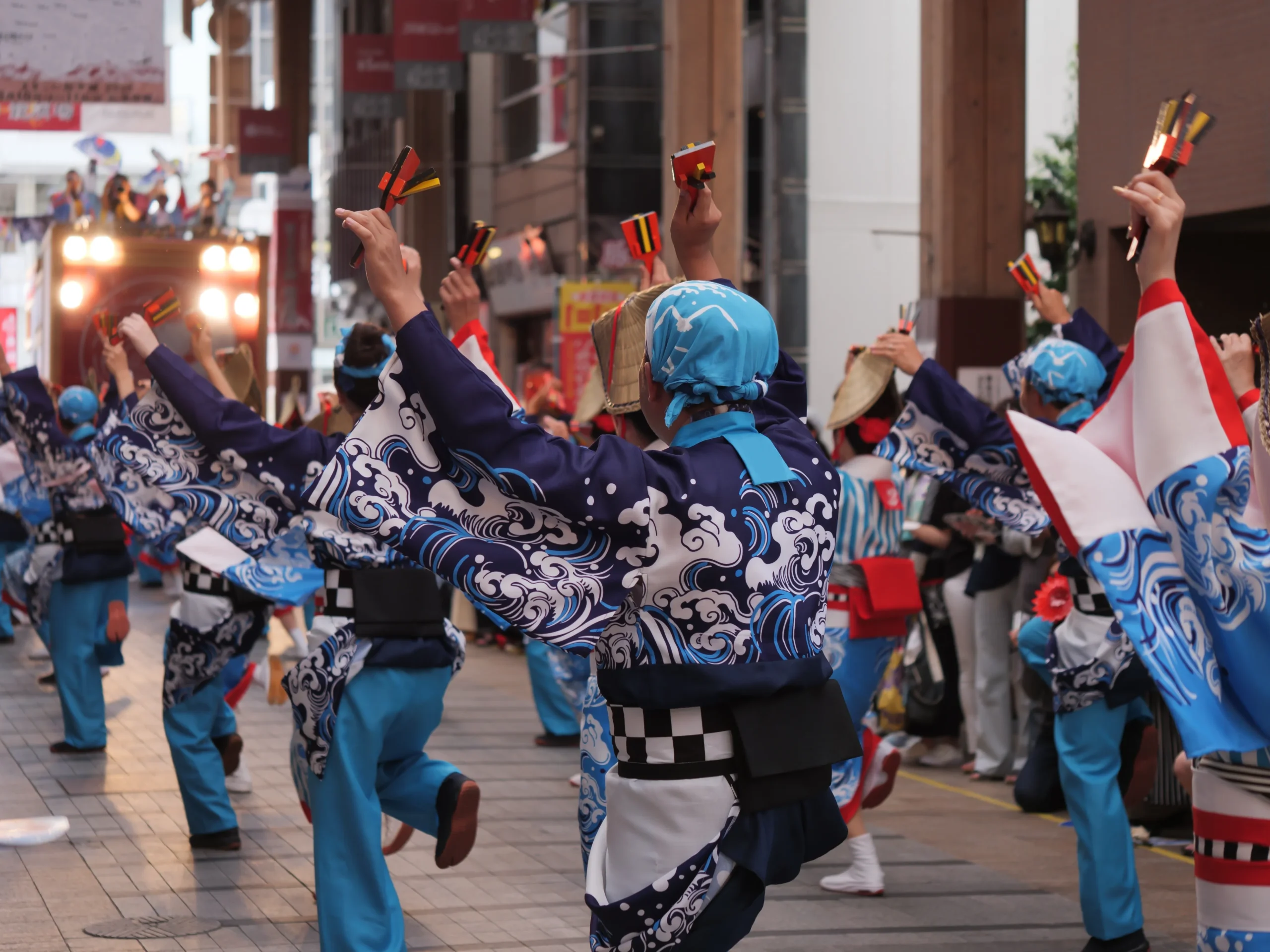 Yosakoi dancers in wave-patterned happi coats holding naruko clappers at a summer festival
