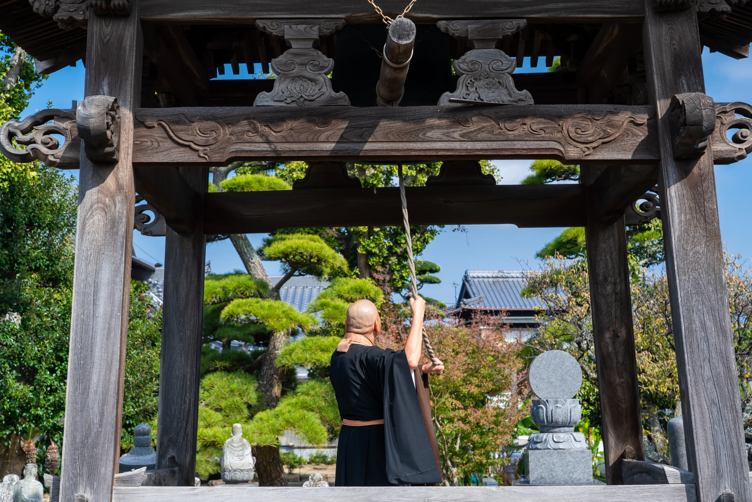 Buddhist monk in black robes pulls the rope to strike a temple bell in a wooden belfry in Japan.