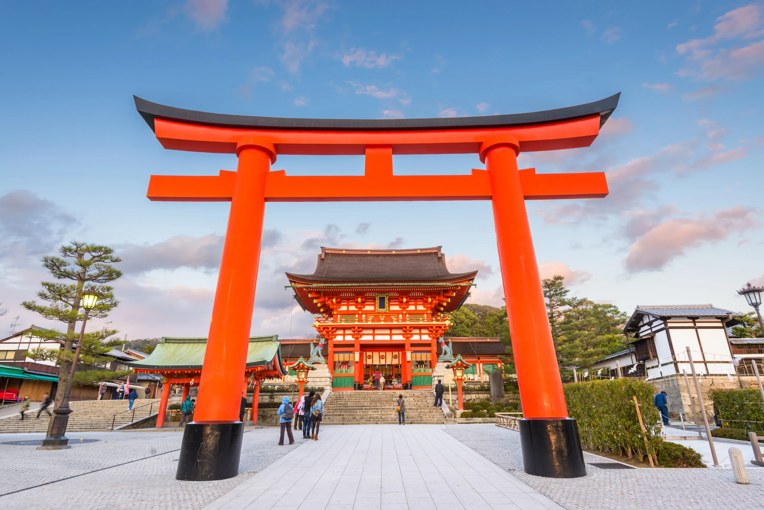 Large vermilion torii gate before the Romon gate at Fushimi Inari Shrine in Kyoto, Japan, at dusk.