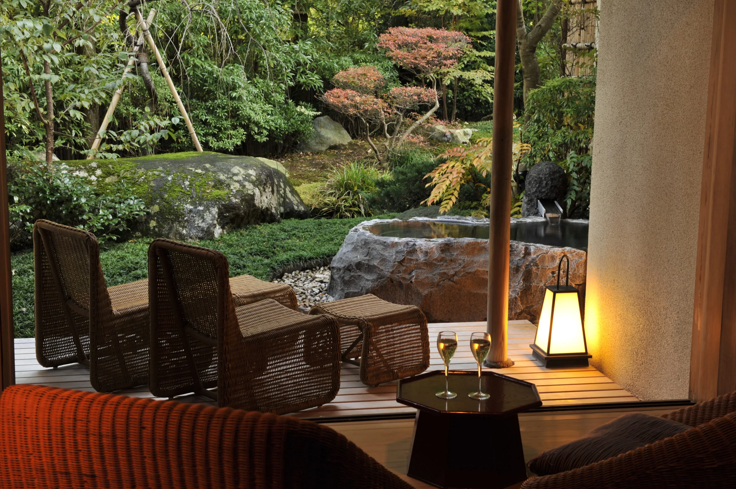 A serene private garden view from Gōra Kadan, featuring wicker lounge chairs, a stone open-air bath, and a cozy lantern-lit atmosphere.
