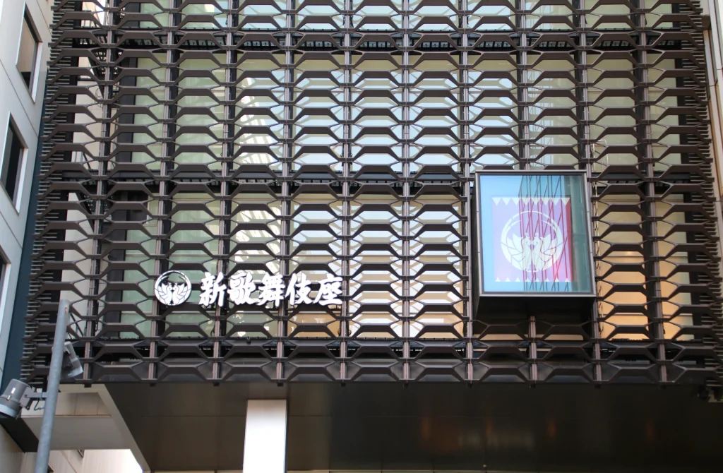 Japanese Shin-Kabukiza lettering above the entrance, with crest-patterned banners displayed in a case.