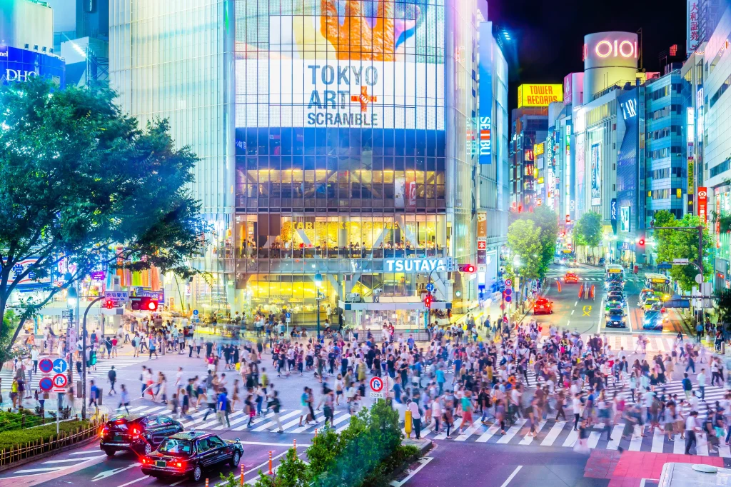 Night view of Shibuya Scramble Crossing in Tokyo, with pedestrians crossing beneath bright digital billboards