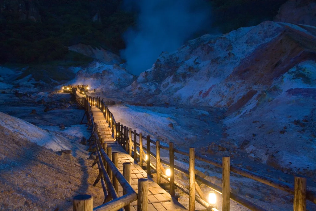 Steam rises from the illuminated volcanic landscape of Jigokudani, Hell Valley, in Noboribetsu Onsen, Hokkaido.