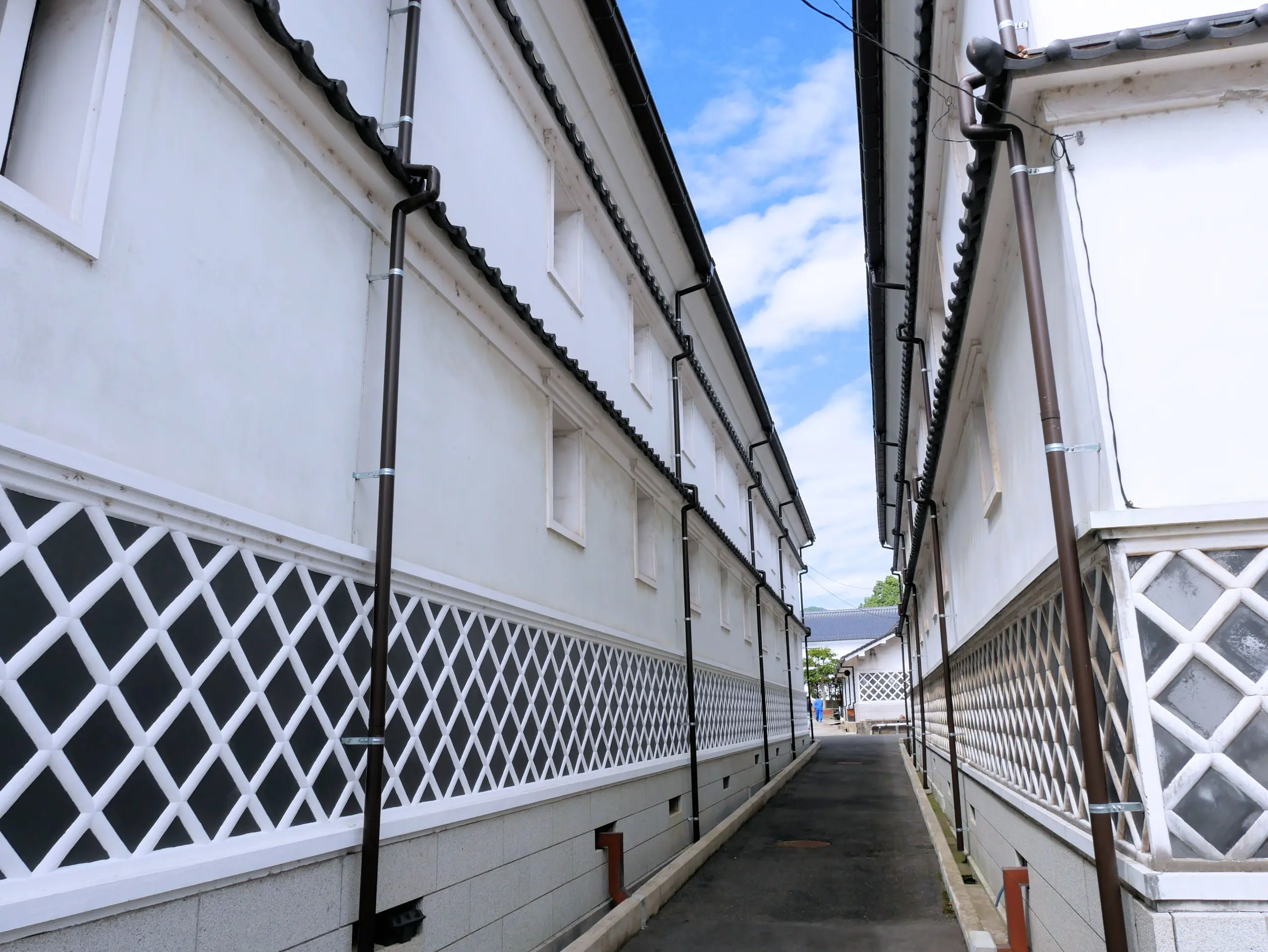 Narrow lane lined with white-walled sake brewery buildings in Saijo.