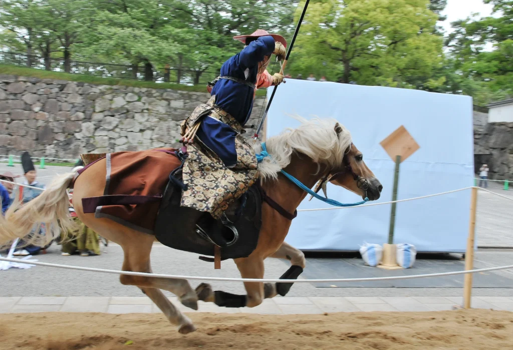 A yabusame archer in traditional clothing shooting an arrow from horseback.