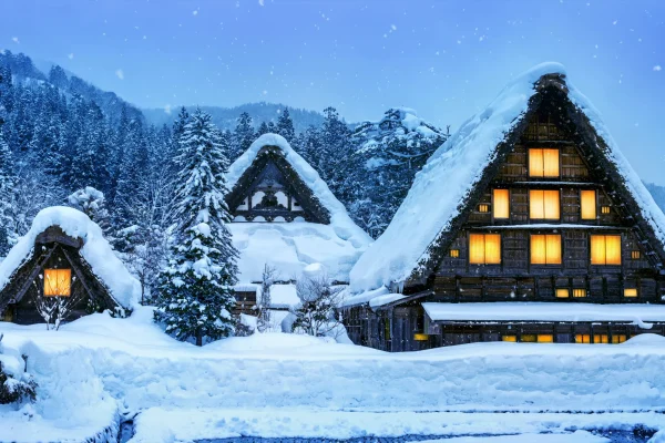 Traditional thatched-roof houses in Shirakawa-go, covered in thick snow with warm glowing lights during winter.
