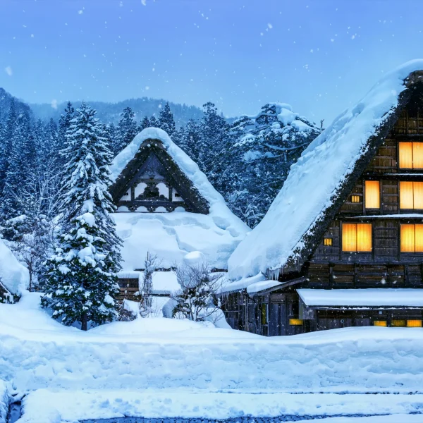 Traditional thatched-roof houses in Shirakawa-go, covered in thick snow with warm glowing lights during winter.