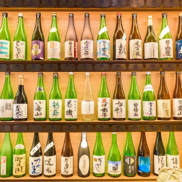 A display of various Japanese sake bottles on wooden shelves, showcasing different labels and brands.